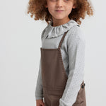 Pige iført brune selebukser og grå strikbluse set forfra