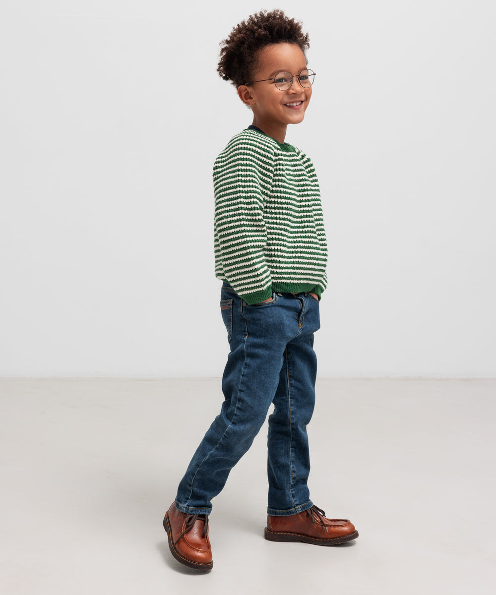 Dreng i grøn stribet striktrøje og jeans set fra siden