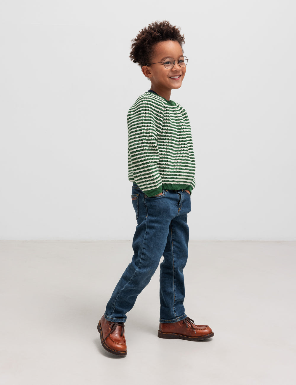 Boy in green striped sweater and jeans seen from the side
