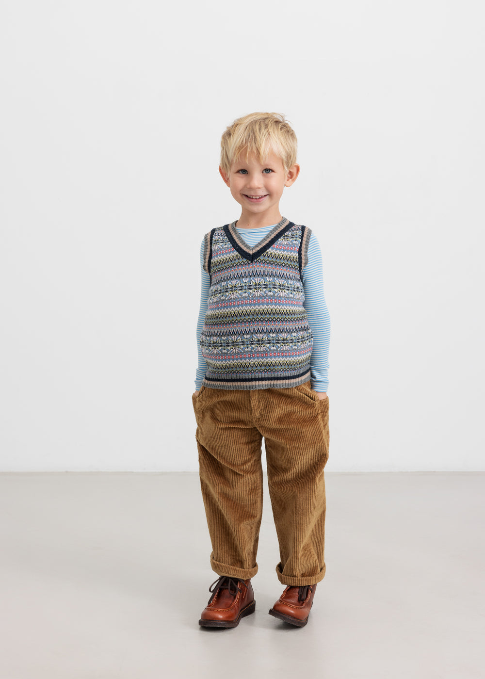 Dreng i brun buks og farverig strikvest med V-hals