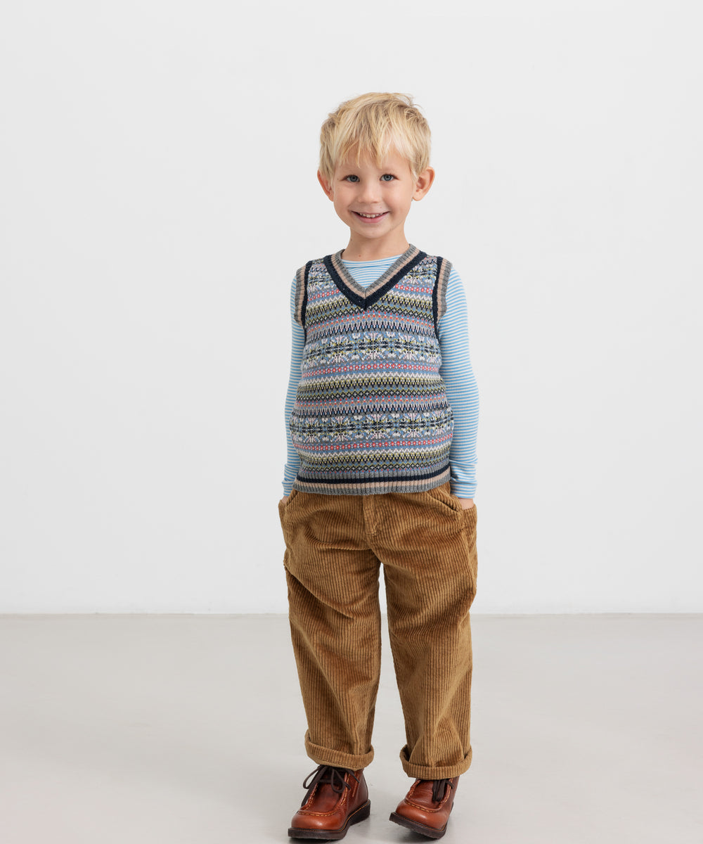 Dreng iført blå og hvid stribet bluse med mønstret strikvest og brune bukser