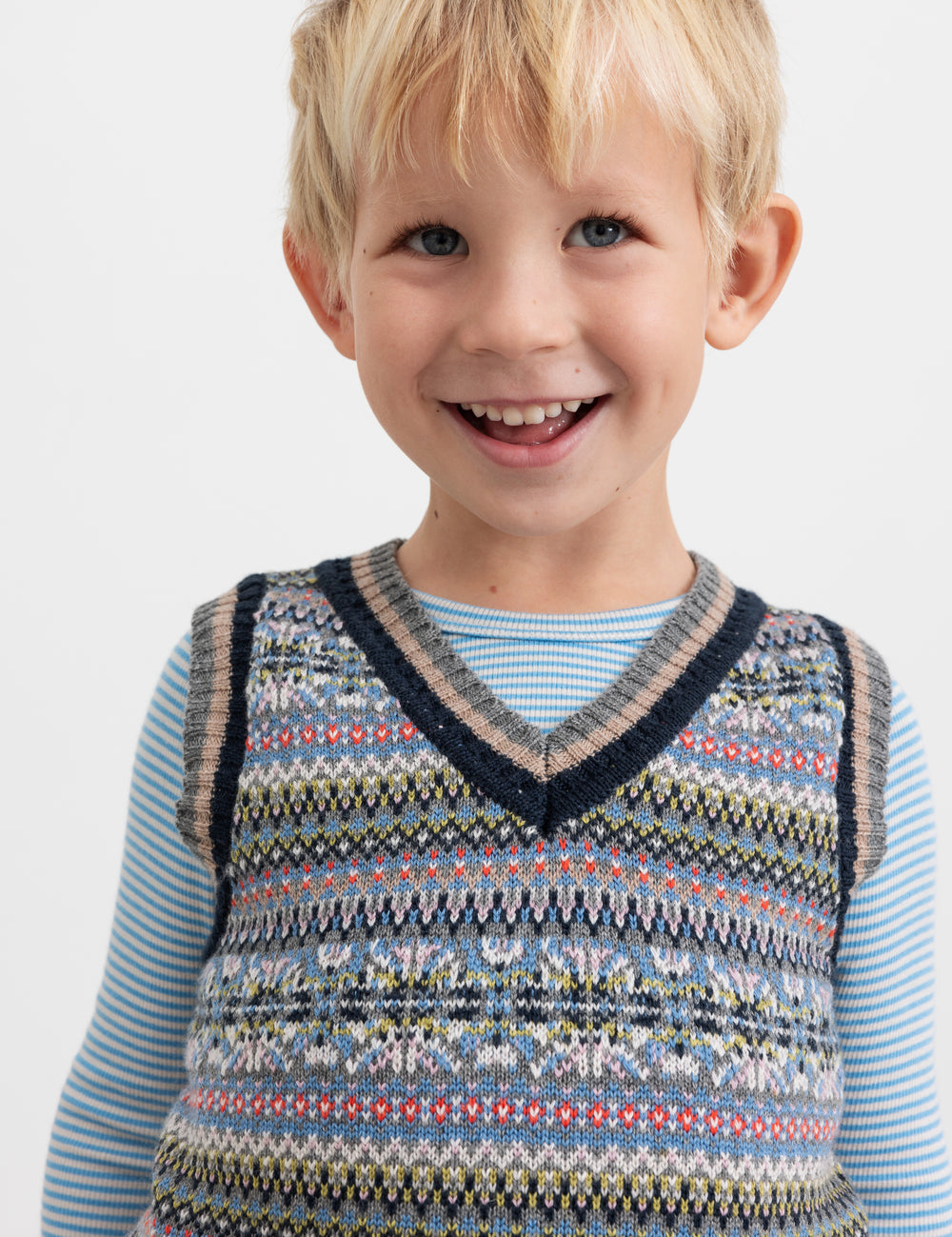 Dreng iført mønstret strikvest over lyseblå bluse.