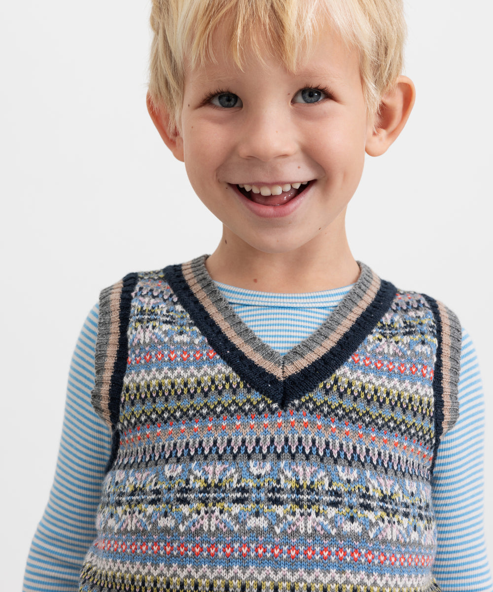 Smilende dreng iført blå og hvid stribet bluse under mønstret strikvest