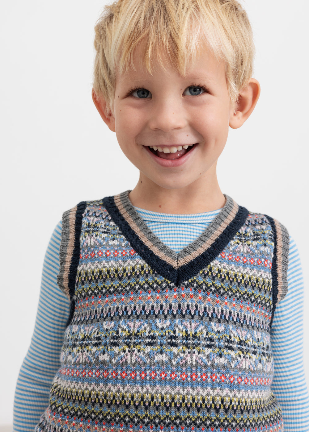 Smilende dreng iført blå og hvid stribet bluse under mønstret strikvest