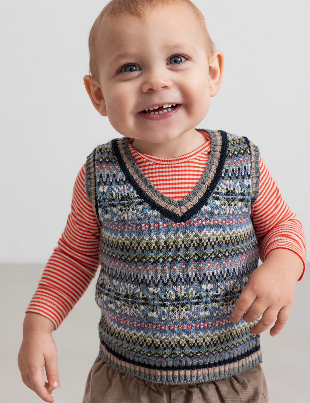 Baby wearing patterned knit vest over striped blouse