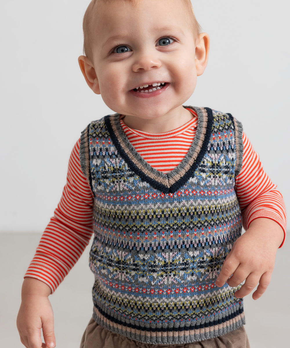 Baby iført rød og hvid stribet body under mønstret strikvest