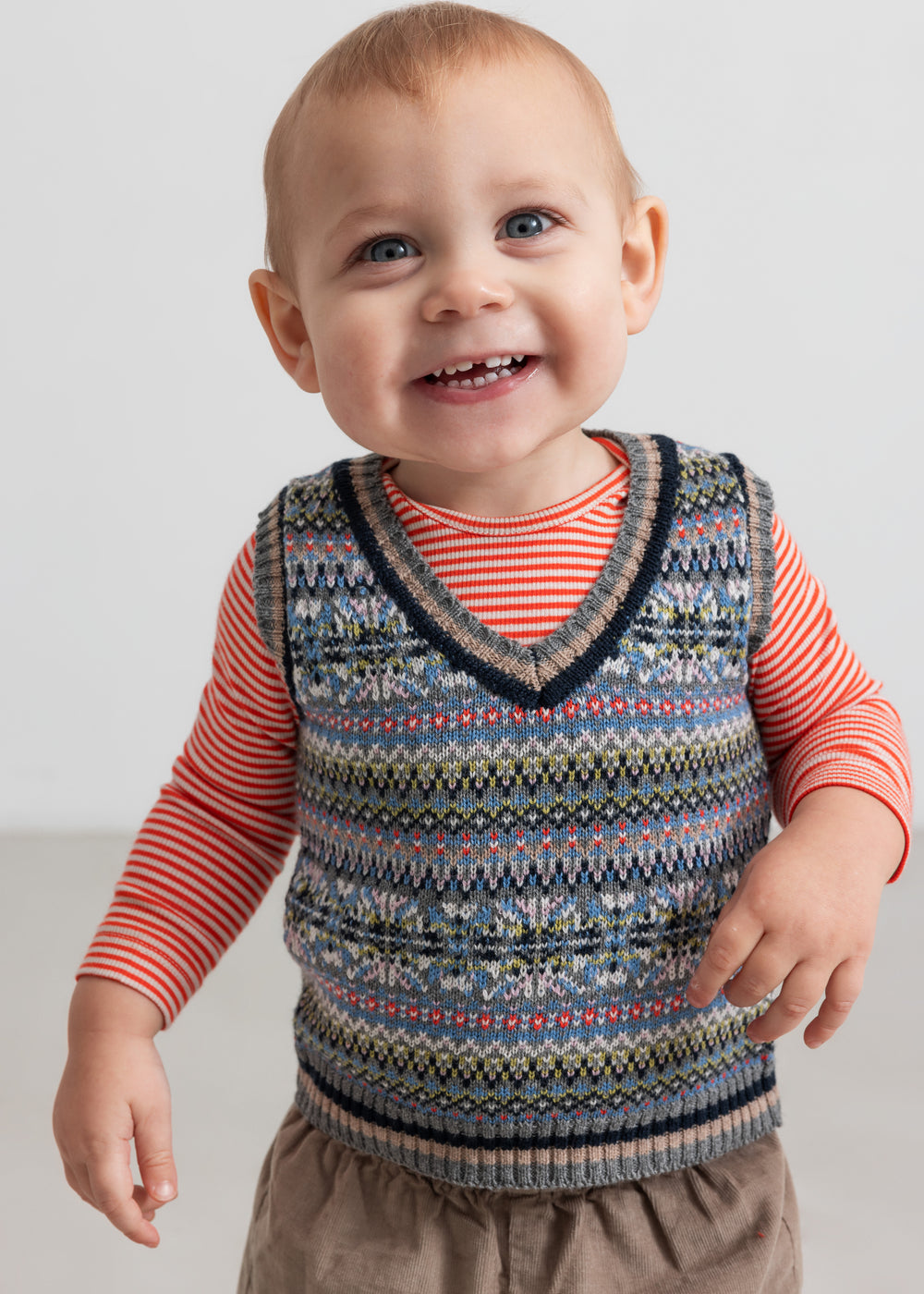 Baby iført rød og hvid stribet body under mønstret strikvest