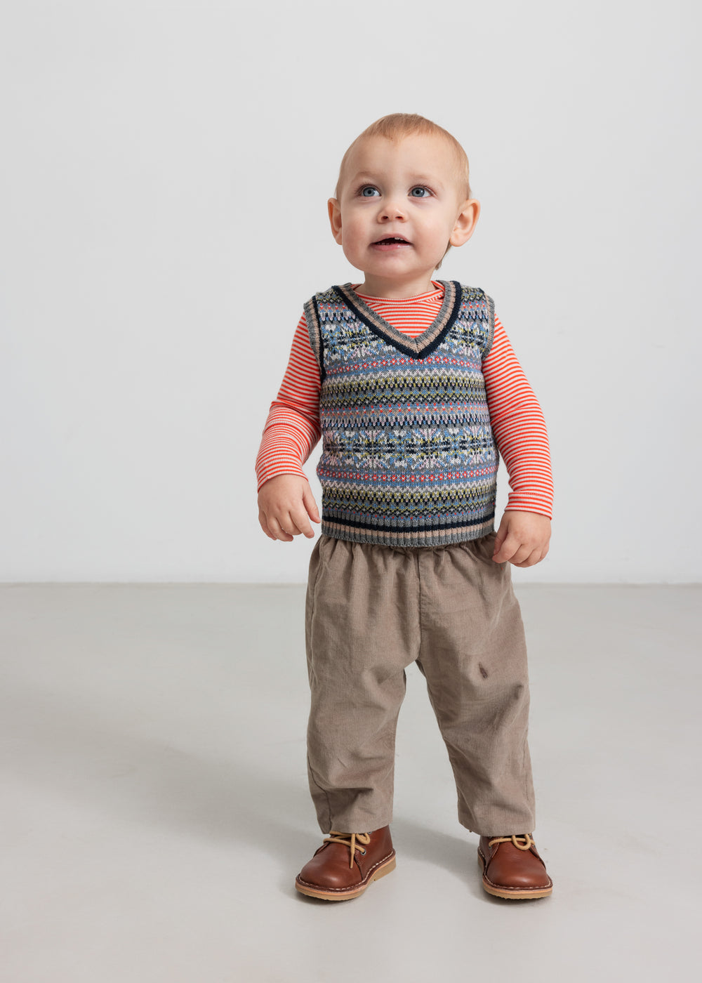 Baby iført mønstret strikvest over stribet bluse