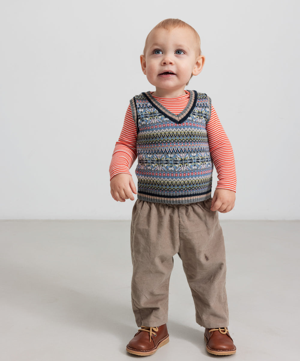 Baby iført beige babyfløjl­sbukser og mønstret strikvest