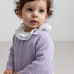 Lille børn med krøllet hår iført lilla strikket trøje og hvid bluse med flæsekant