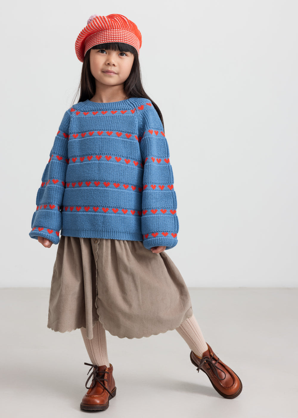 Børn i blå strikbluse og rød beret med kvast