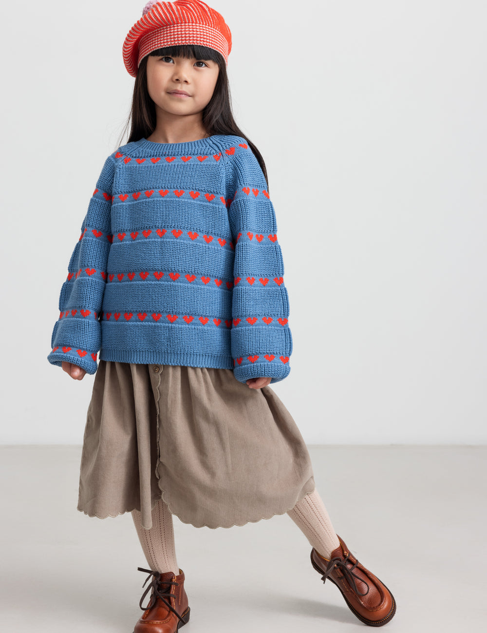 Children wearing blue sweater with red hearts, combined with brown skirt and red hat