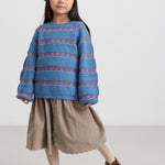 Pige iført beige babyfløjl­s­nederdel og stribet blå bluse