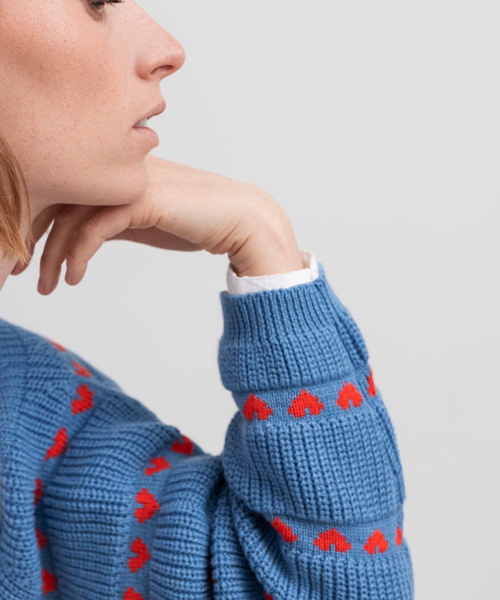 Kvinde iført blå striktrøje med røde hjerter og lange ærmer