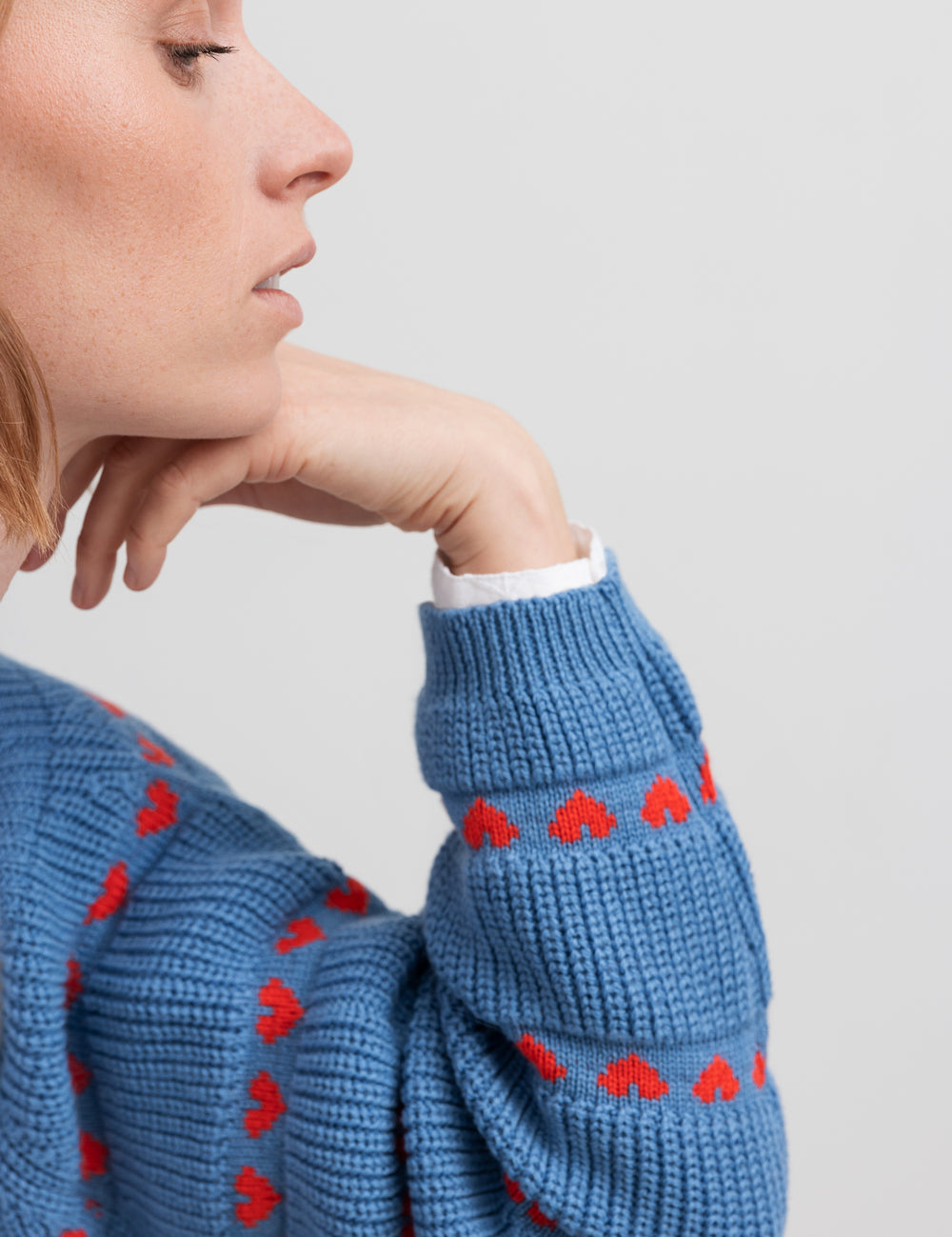 Kvinde iført blå striktrøje med røde hjerter og lange ærmer