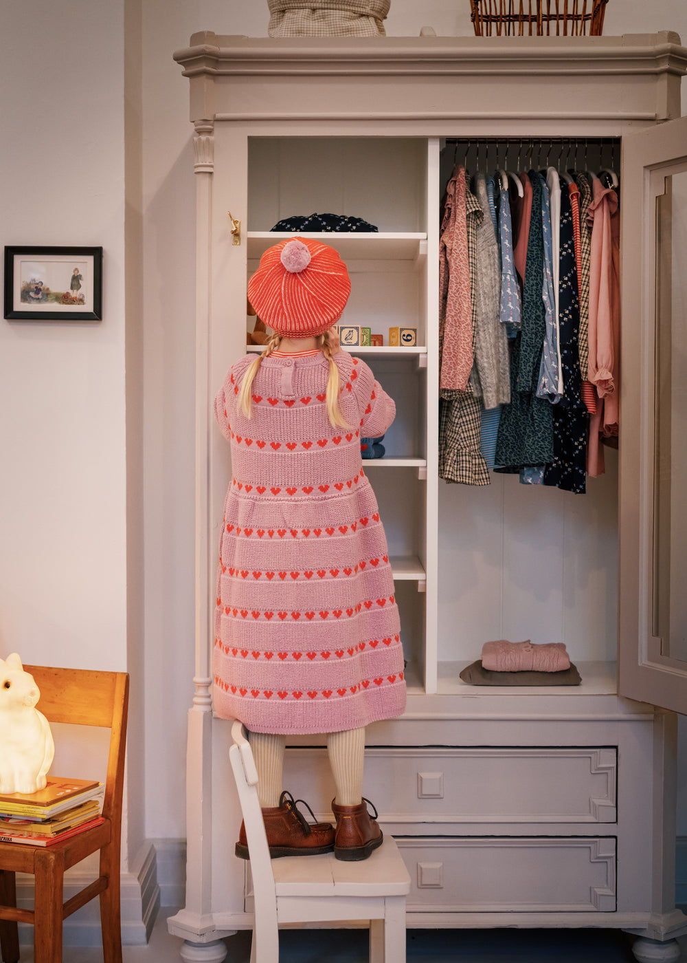 Barn i lyserød strikkjole med røde hjerter kigger i klædeskab