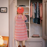 Barn i lyserød strikkjole med røde hjerter kigger i klædeskab