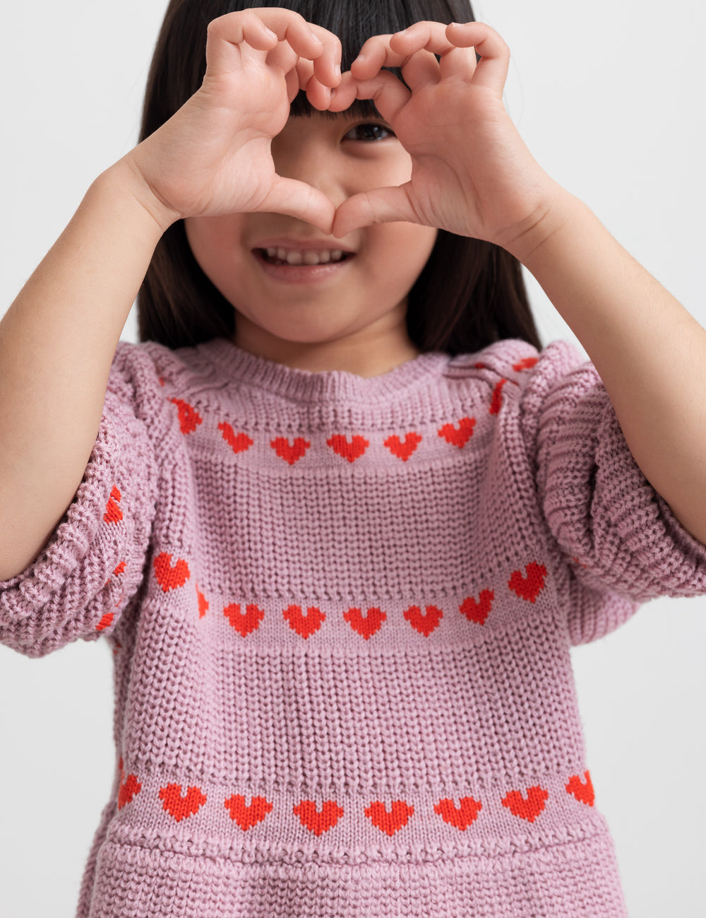 Pige iført lyserød strikkjole med røde hjerter