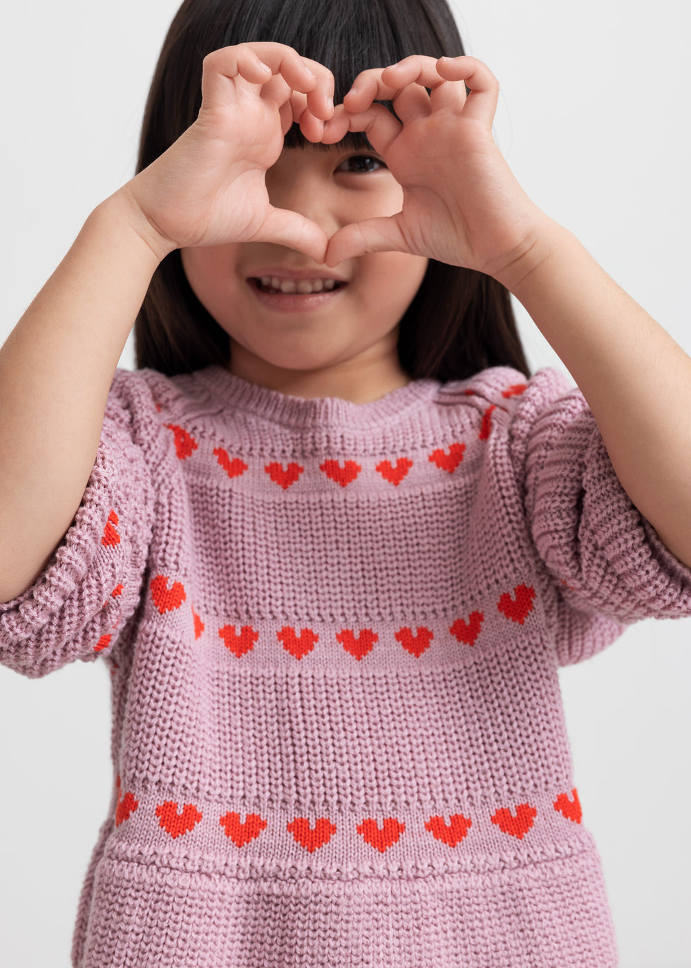 Pige iført lyserød strikkjole med røde hjerter