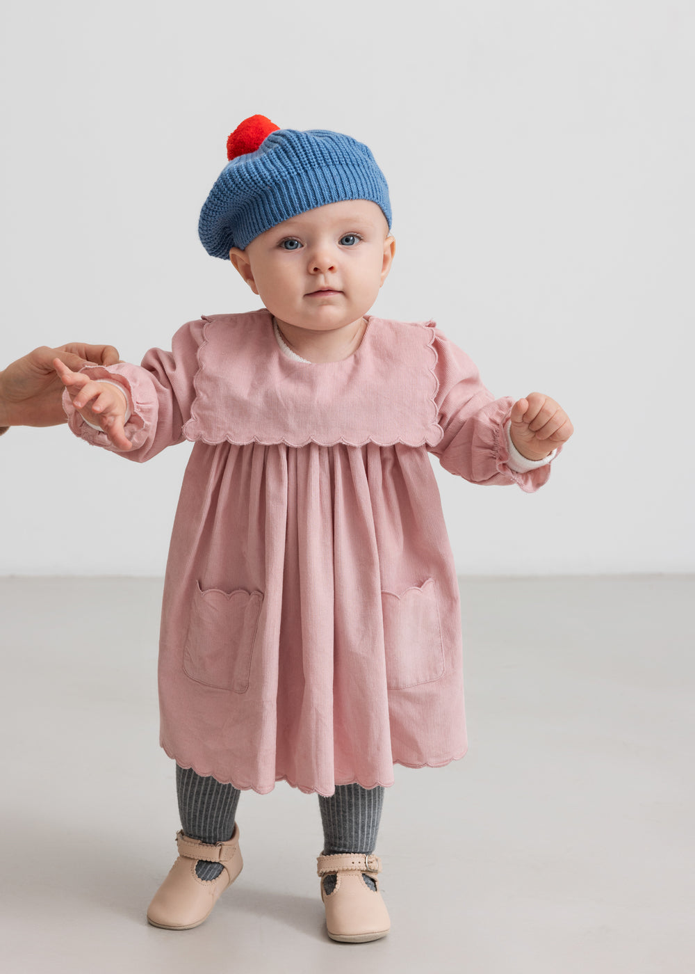 Baby i rosa kjole med blå strikket beret med rød kvast