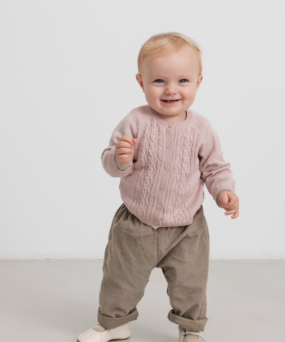 Børn iført lyserød strikcardigan og beige bukser, stående