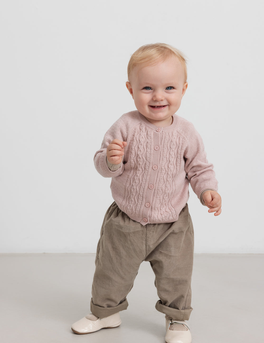 Children wearing pink knitted cardigan and beige pants, standing
