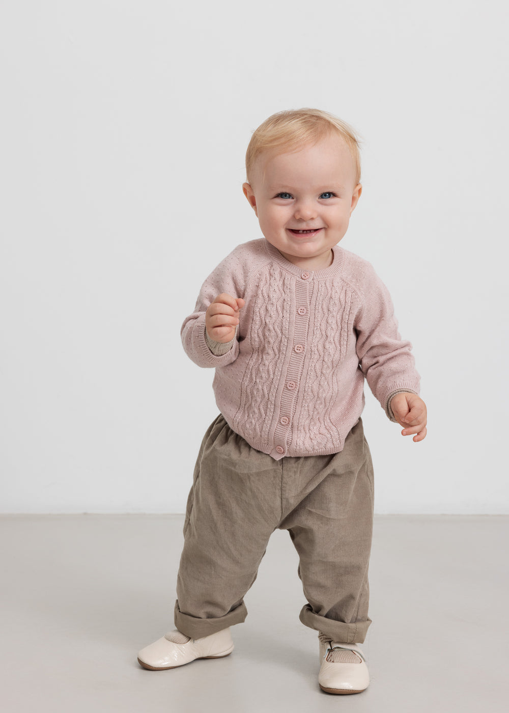 Baby i beige babyfløjl­sbukser og lyserød trøje