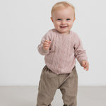 Baby i beige babyfløjl­sbukser og lyserød trøje