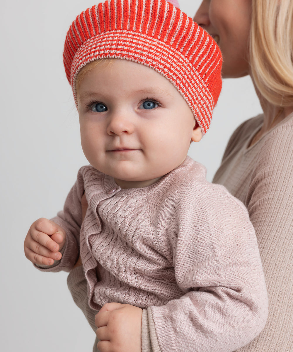 Baby iført lyserød strikcardigan og orange hue, tæt på