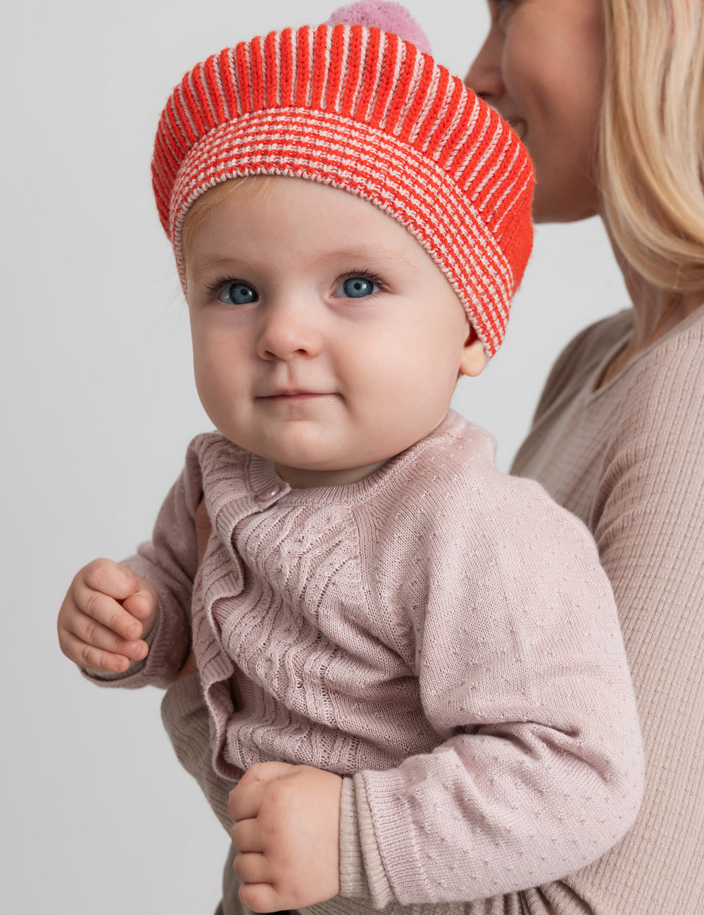 Baby wearing pink knitted cardigan and orange hat, close-up