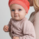 Baby iført lyserød strikcardigan og orange hue, tæt på