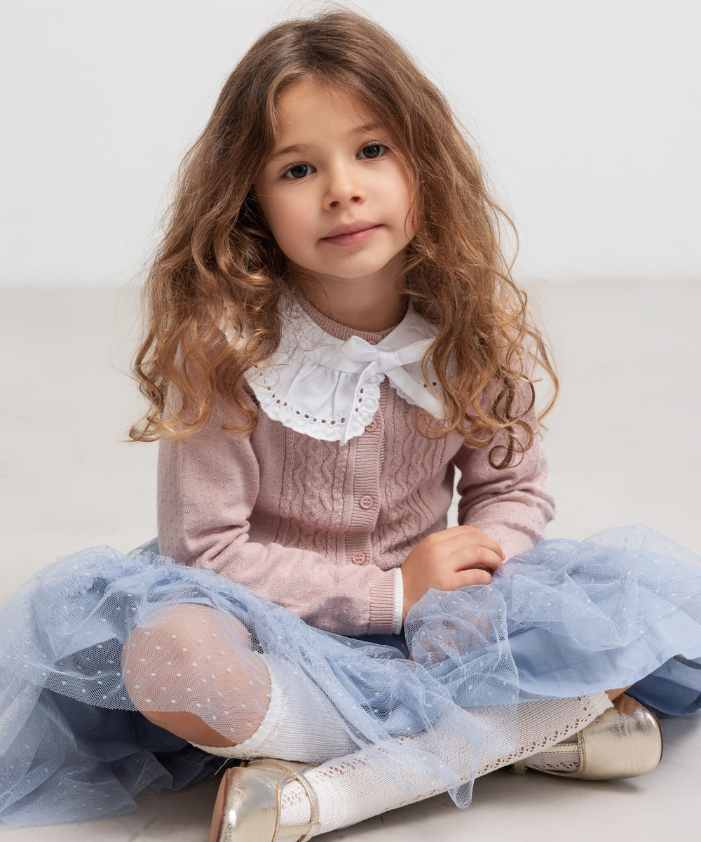 Pige sidder iført blå tylnederdel med prikmønster og bluse