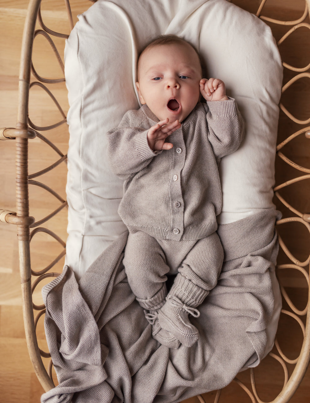 Baby with open mouth in beige knitted set lying in basket