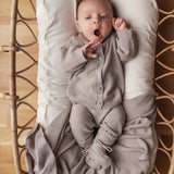 Baby iført beige/grå strikket sæt liggende i flettet kurv med beige tæppe