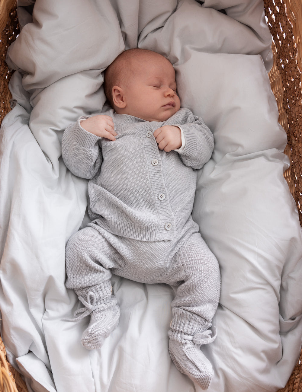 Sleeping baby in light gray knitted set lying in basket
