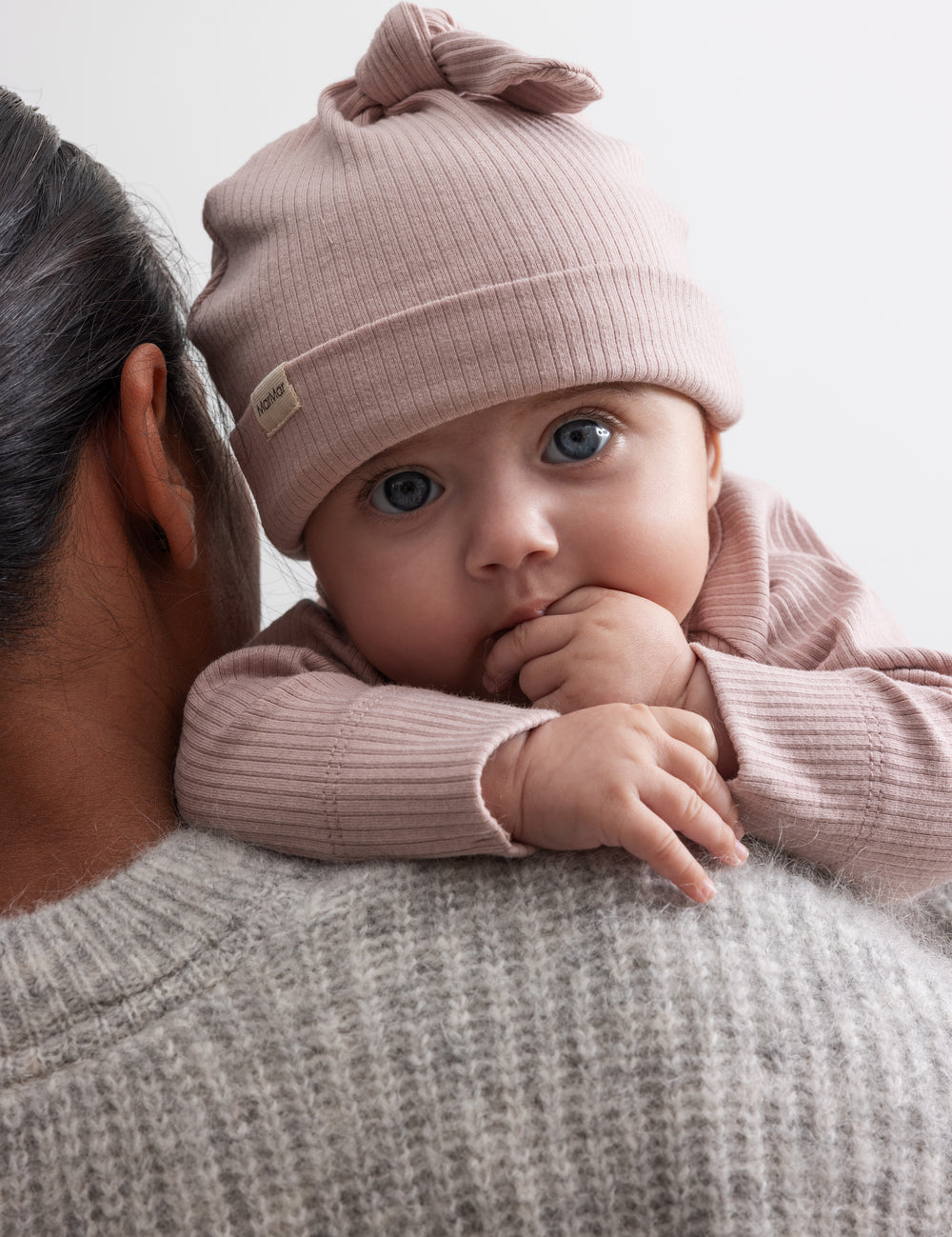Baby med lyserød ribstrikket babyhue, knude på toppen og opbukket kant
