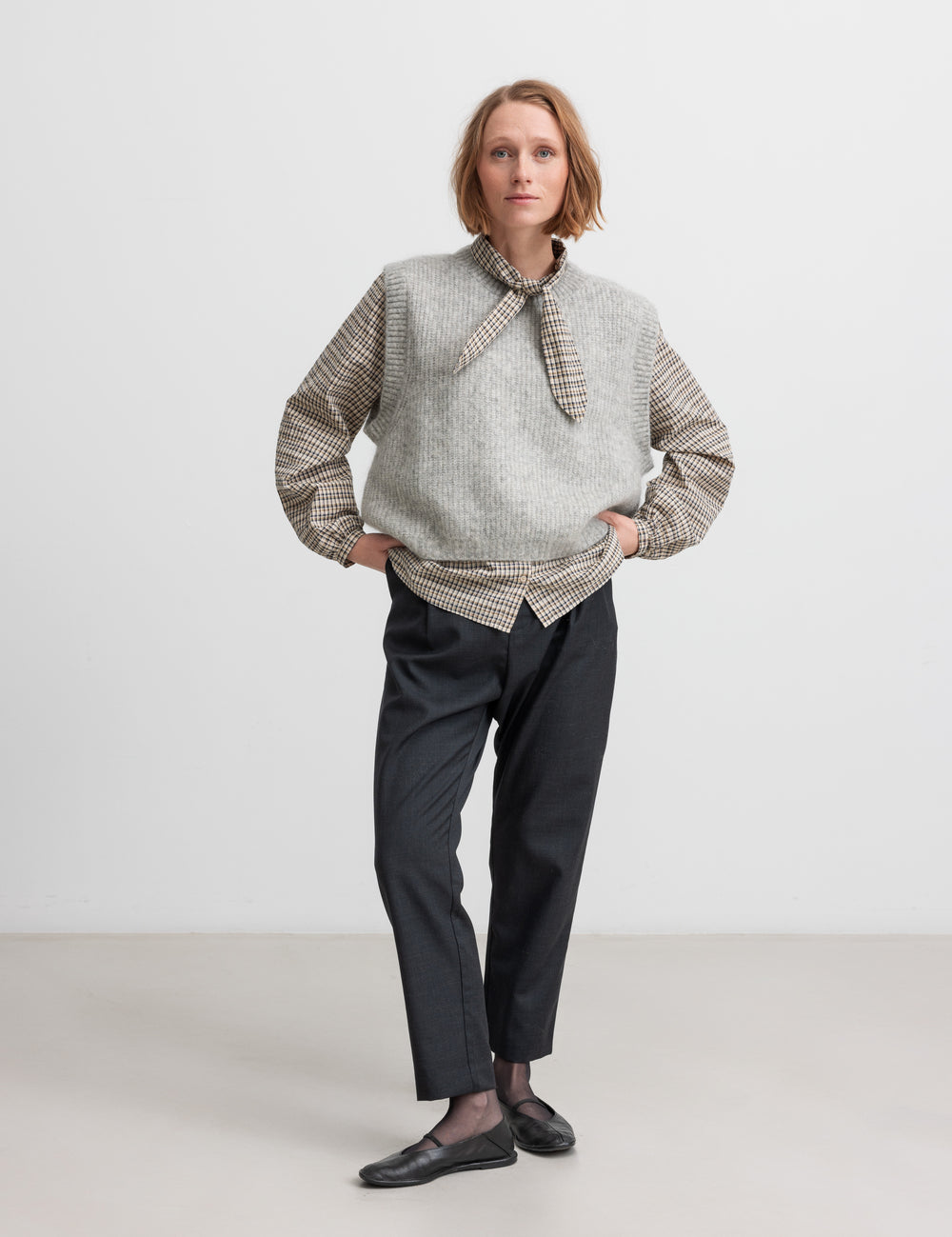 Kvinde iført grå strikvest i uld stylet med skjorte og bukser