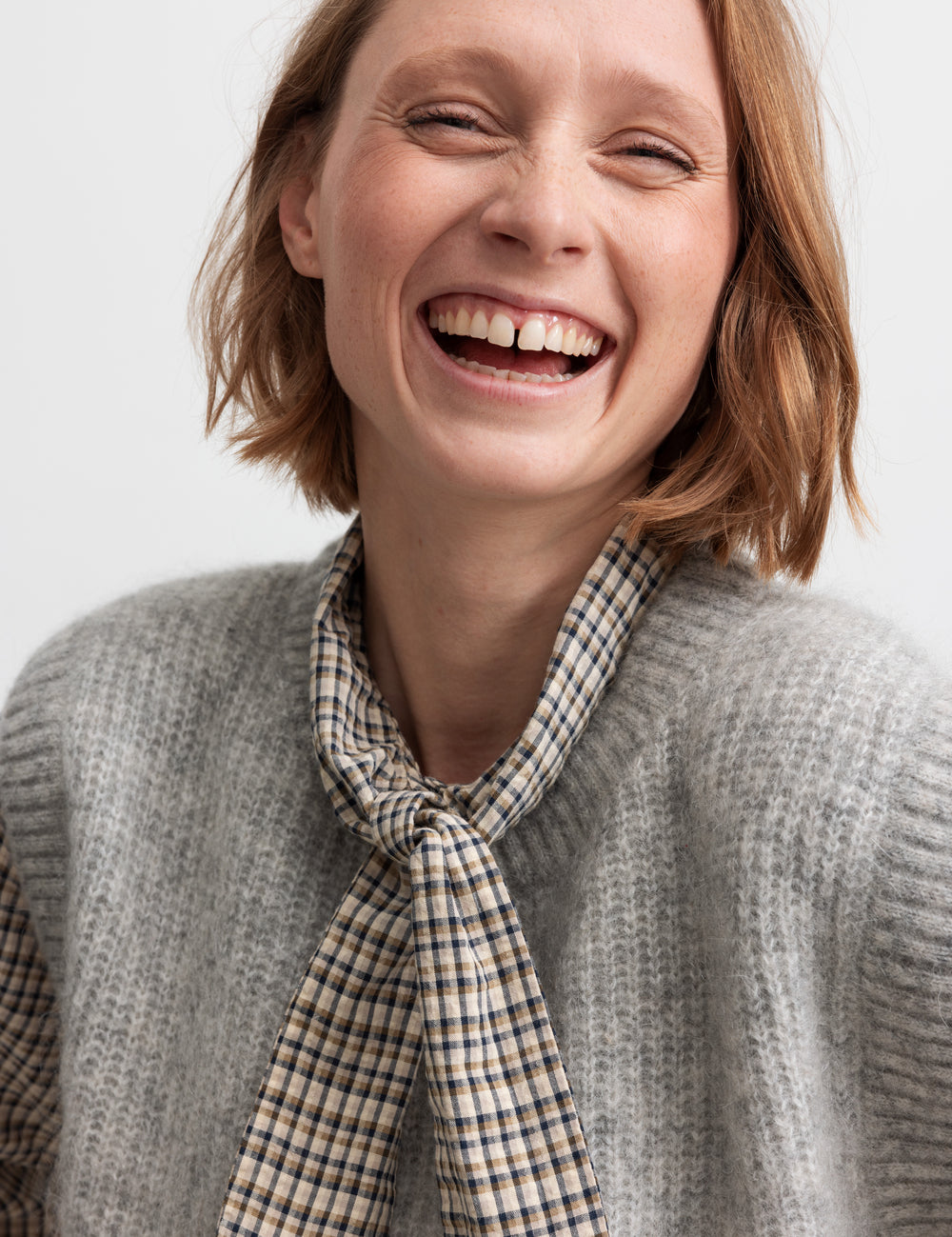 Kvinde smilende i grå strikvest af uld med skjorte under