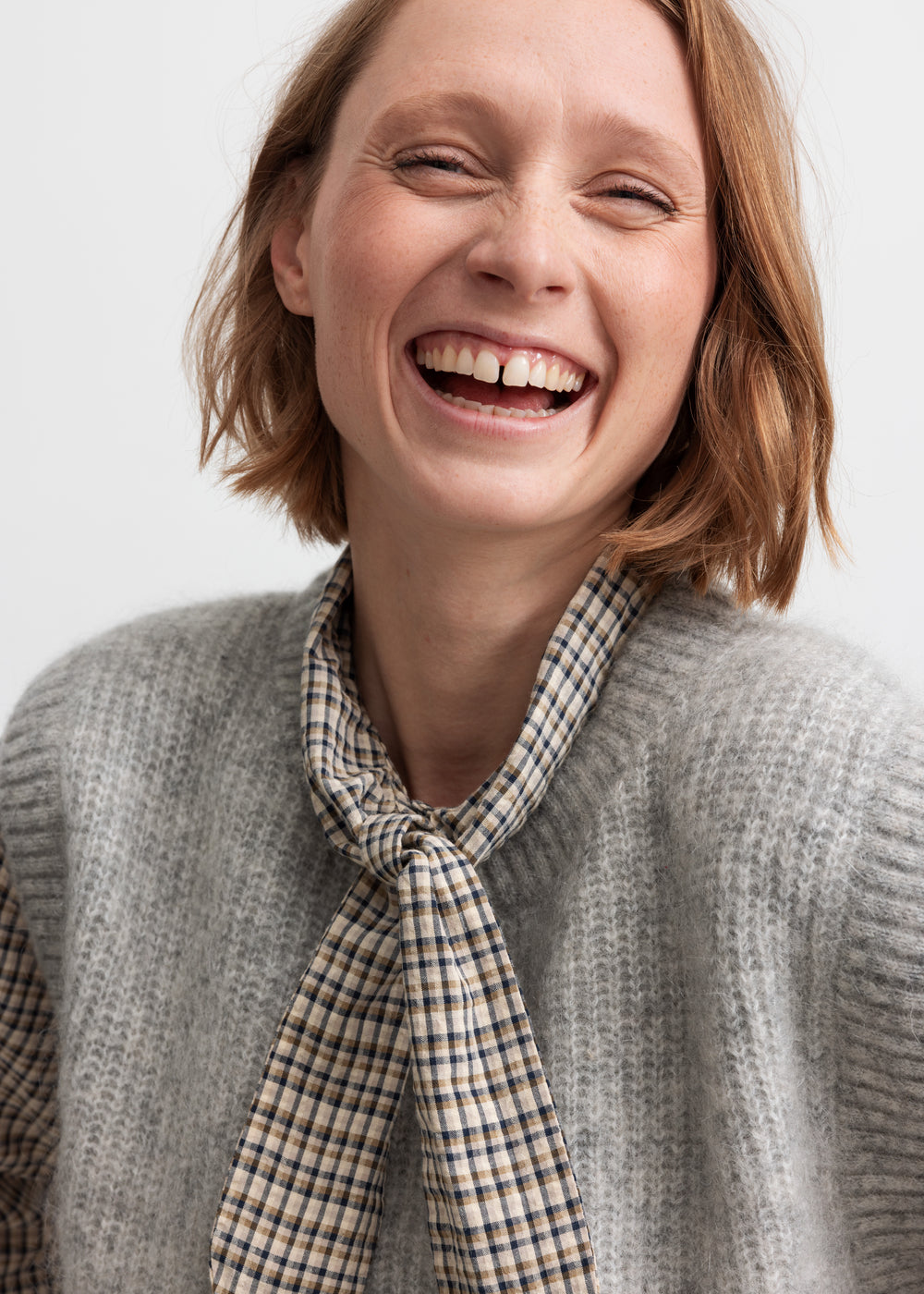 Kvinde smilende i grå strikvest i uld med skjorte under