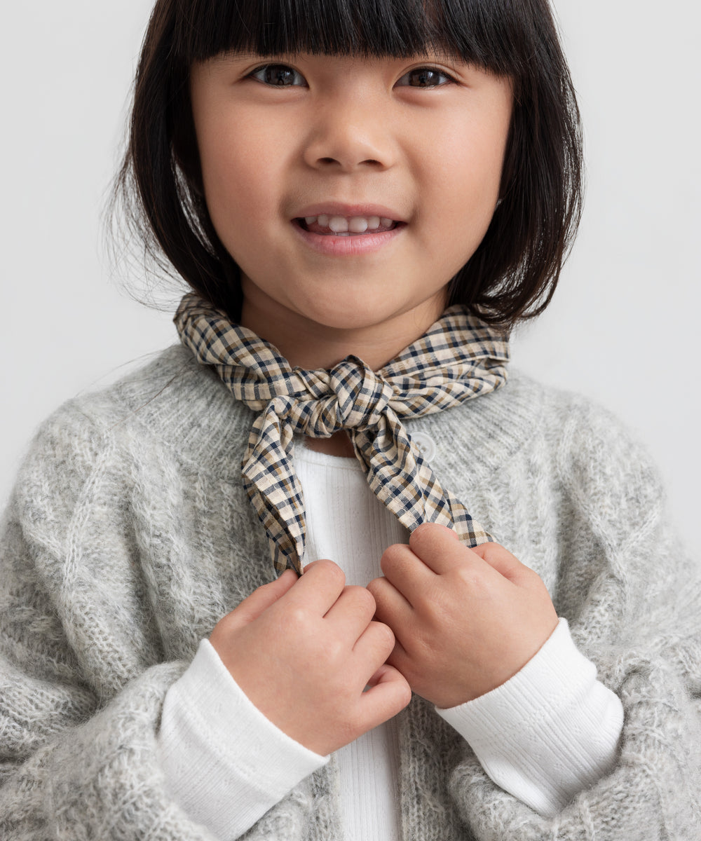 Pige iført hvid pointelle bluse, grå cardigan og ternet tørklæde