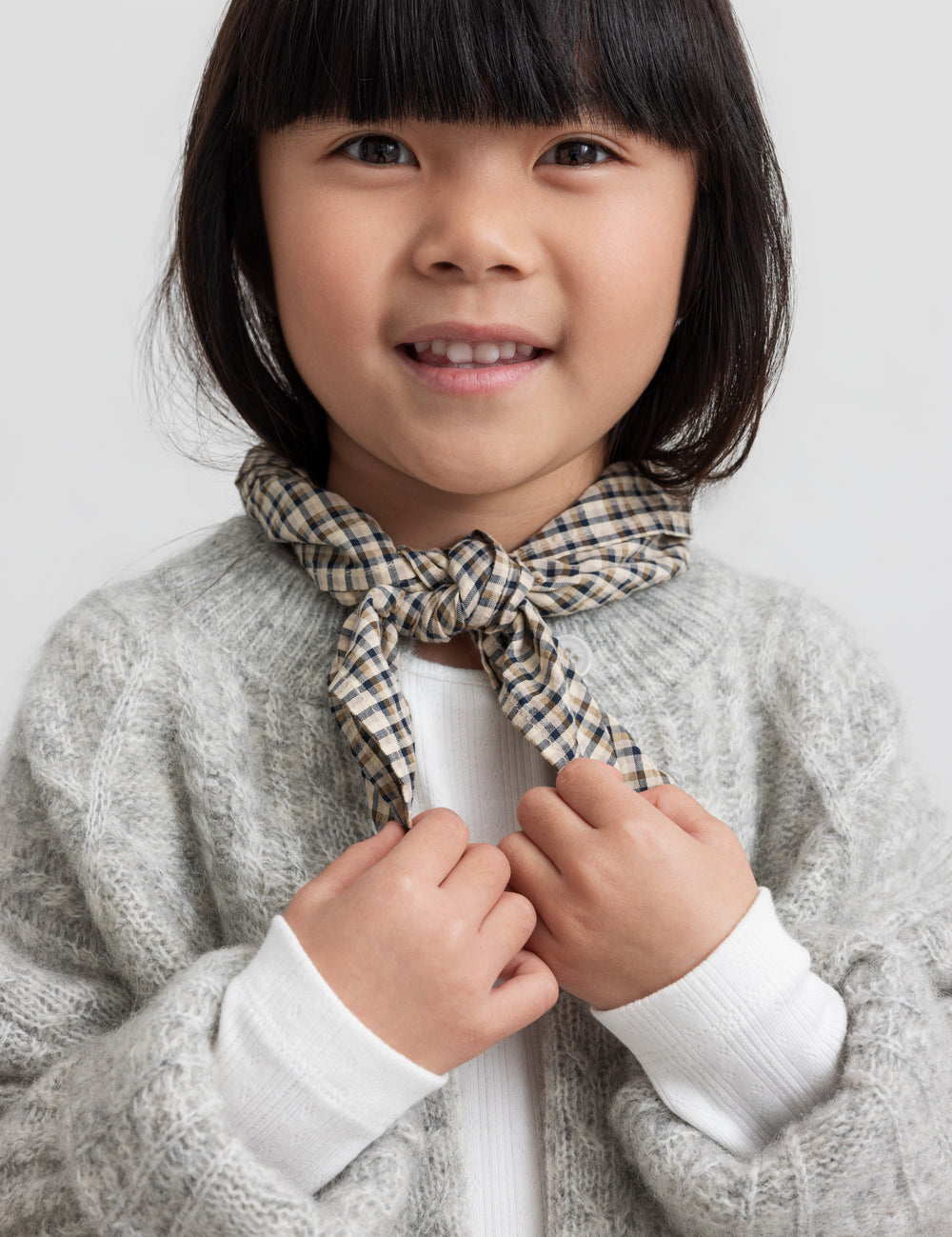 Pige iført hvid pointelle bluse, grå cardigan og ternet tørklæde.