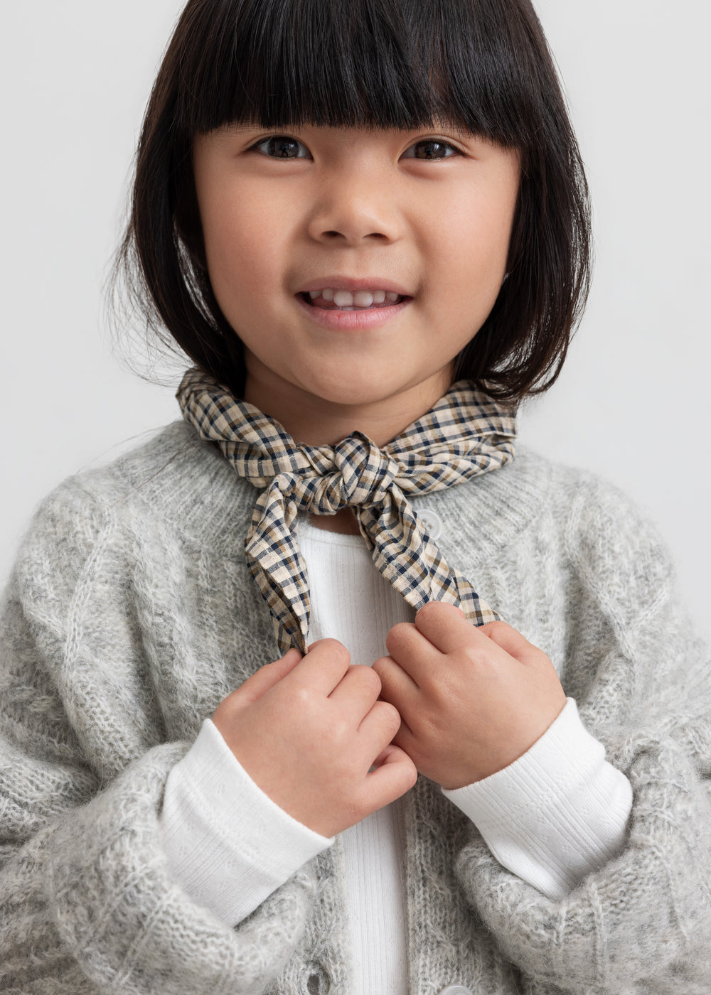 Pige iført lysegrå cardigan med ternet tørklæde