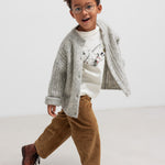 Dreng iført lysegrå cardigan og brune bukser