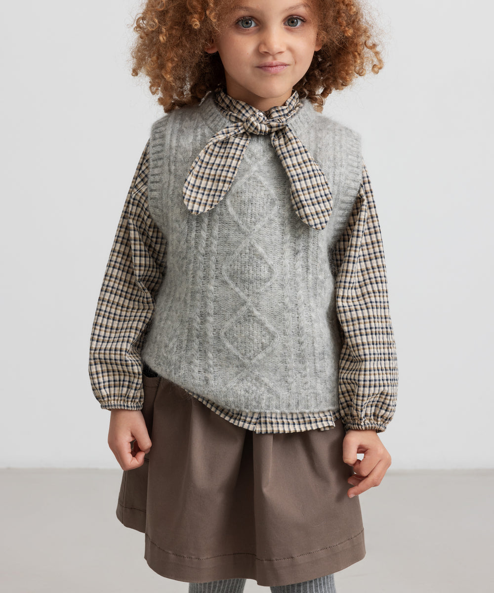 Børn iført kaki nederdel og strikvest set forfra