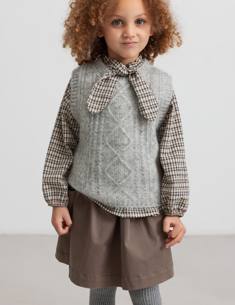 Children wearing khaki skirt and knitted vest seen from the front