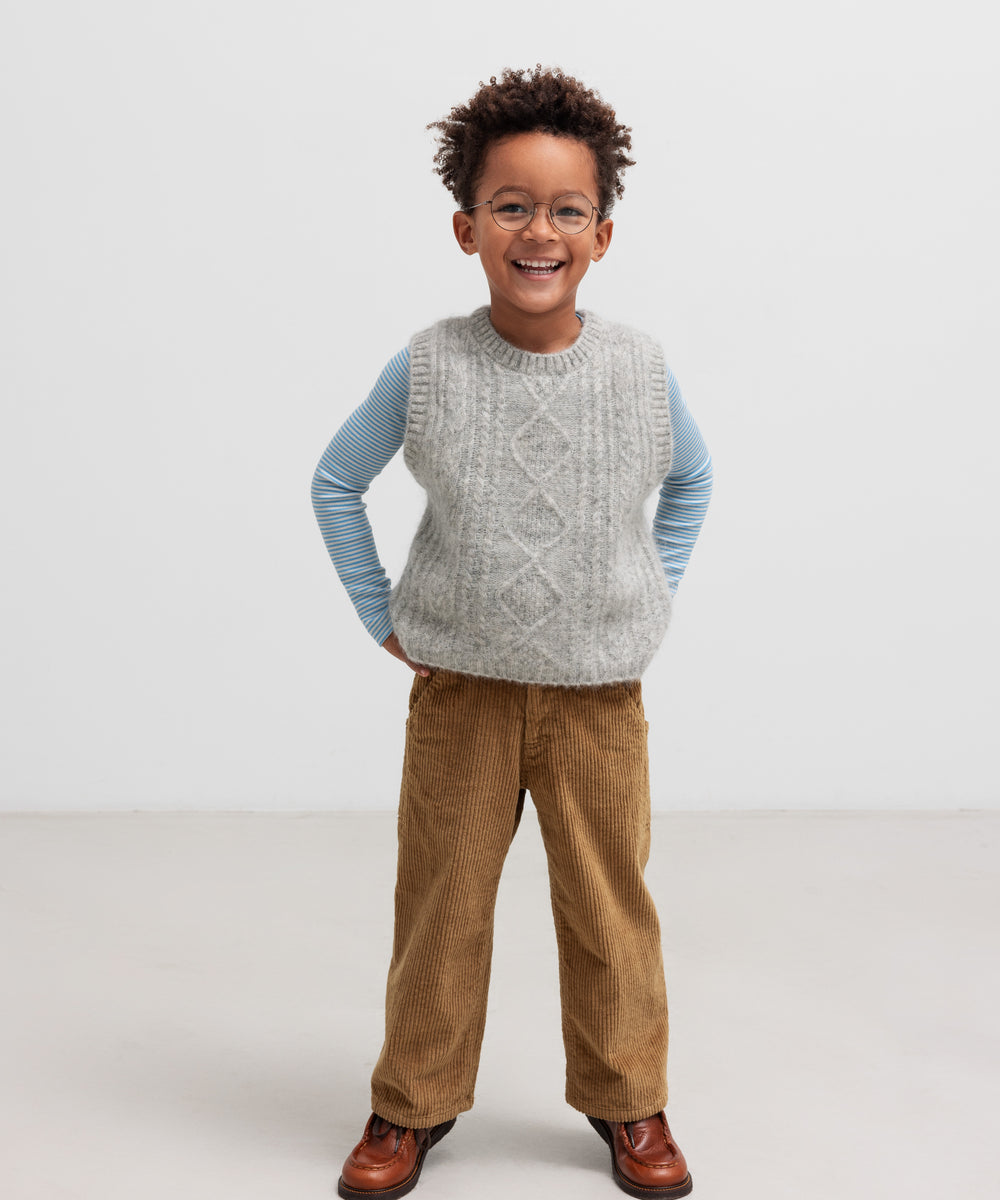 Dreng iført blå og hvid stribet bluse med grå strikvest og brune bukser