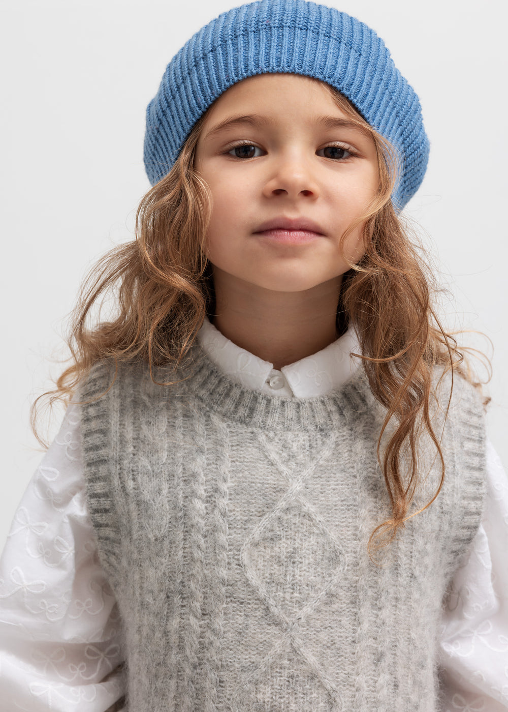 Pige med blå beret og rød kvast iført grå vest og hvid skjorte