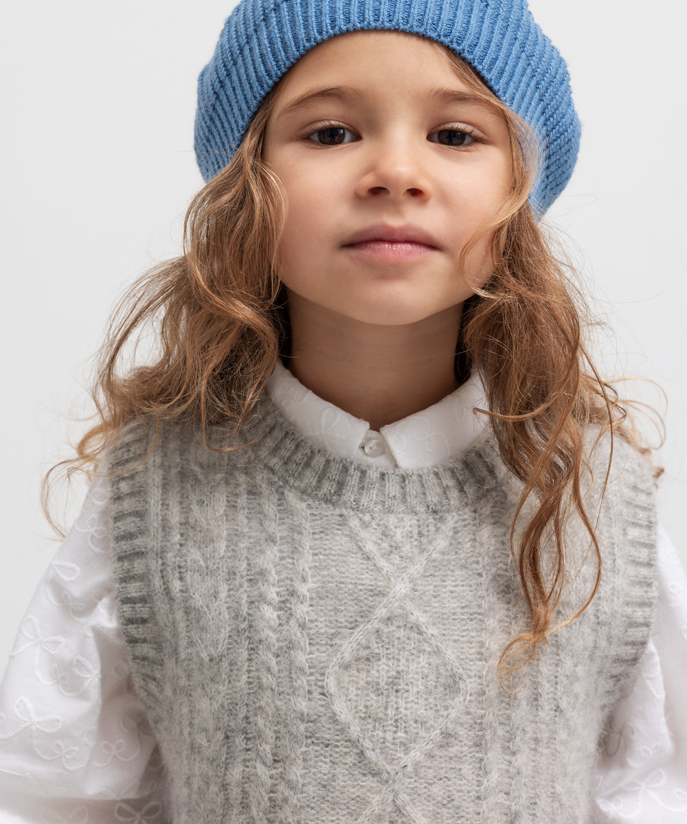 Børn med blå hue, grå strikket vest og hvid bluse