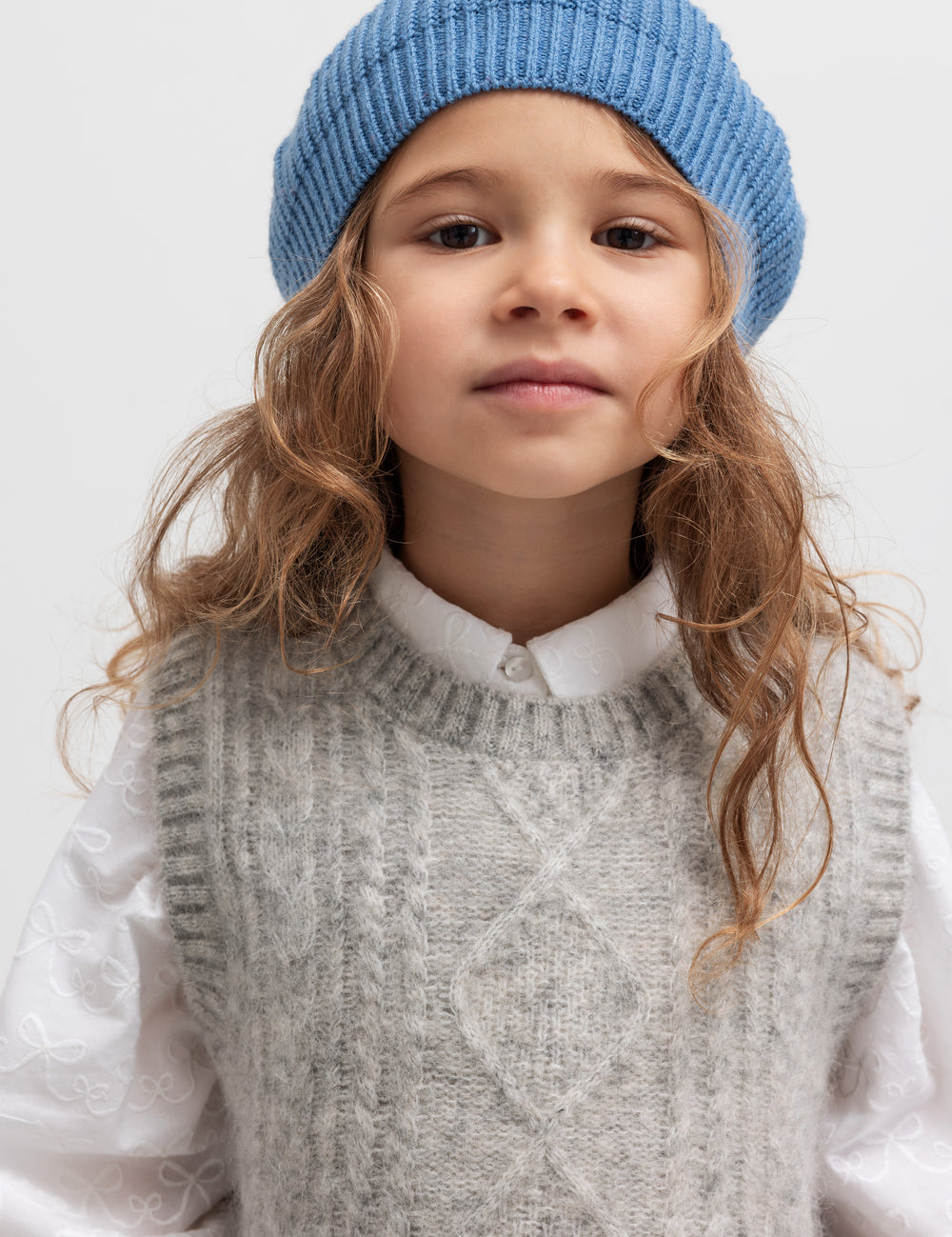 Børn iført grå strikvest over hvid skjorte og blå hue