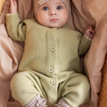 Baby iført blødt beige strikket heldragt med knapper foran